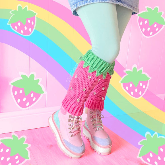 A woman is shown wearing a denim miniskirt, pastel green leggings, crochet bubblegum pink and pastel green leg warmers designed to look like a strawberry and pastel platform boots. The background has an illustrated wiggly pastel rainbow and pastel strawberries