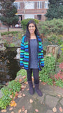 Parveen wears a VelvetVolcano custom striped cardigan in a palette of green and blue shades with black accents.
