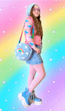 Tamsyn, a white woman with long wavy brown hair wearing a duck egg blue crochet beret and matching circular shoulder bag with pastel rainbow and white cloud design, a pink long sleeved top with colourful cartoon rabbit design, a bubblegum pink denim vest, light wash denim mini skirt, baby pink leggings, blue platform ankle boots with glittery butterfly wings and white chunky soles and lilac heart shaped glasses.