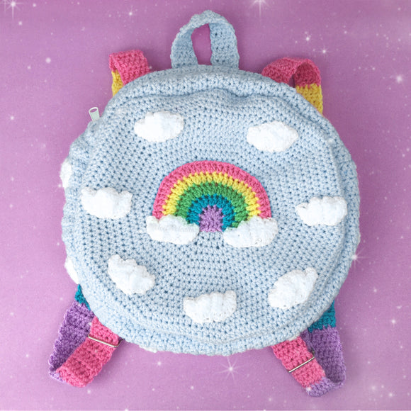 Light blue crochet circular backpack with pastel rainbow striped straps and a pastel rainbow and cloud design on the front by VelvetVolcano
