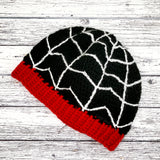 Black fitted crochet beanie with white spider web / cobweb design and red ribbed brim by VelvetVolcano