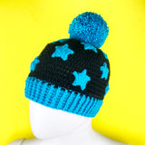 A black crocheted hat with turquoise pom pom, turquoise ribbed brim and a turquoise star applique pattern by VelvetVolcano