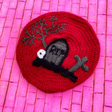 Burgundy crochet beret with graveyard scene in black grey including a cross, gravestone, tree and skull. Graveyard Beret (Custom Colour) by VelvetVolcano