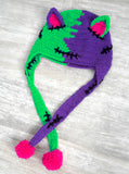 Half neon green, half violet Frankenstein's Monster inspired crochet cat ear, ear flap beanie with neon pink inner ears and pom poms. Custom Colour FrankenKitty Ear Flap Beanie by VelvetVolcano