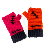 VelvetVolcano FrankenKitty crochet fingerless gloves. One glove is hot pink, the other is orange. Both feature bubblegum pink heart shaped paw prints, black Frankenstein's Monster inspired stitches and black cuffs.