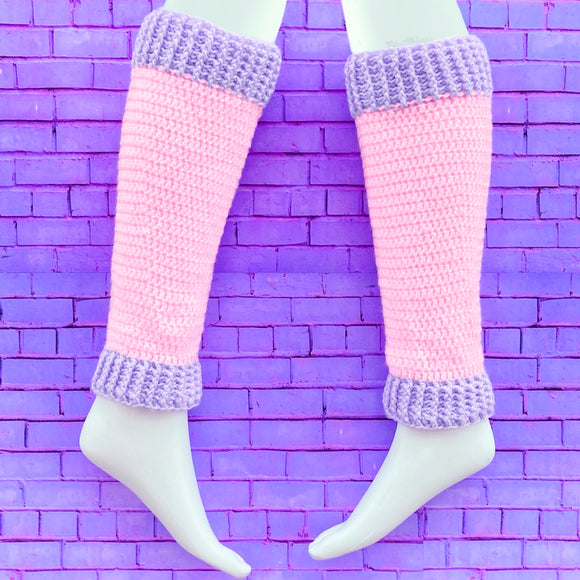 A pair of crochet leg warmers in baby pink with lavender cuffs by VelvetVolcano. The background is purple brick.