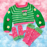 An emerald green and pastel green striped cropped crochet sweater with frog, daisy and strawberry appliques, bubblegum pink and pastel green strawberry mittens and matching leg warmers.