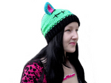 Tamsyn, a white woman with long black hair is wearing a zombie cat inspired "FrankenKitty Beanie", a hot pink and black leopard print cardigan and a black t-shirt with ribcage print