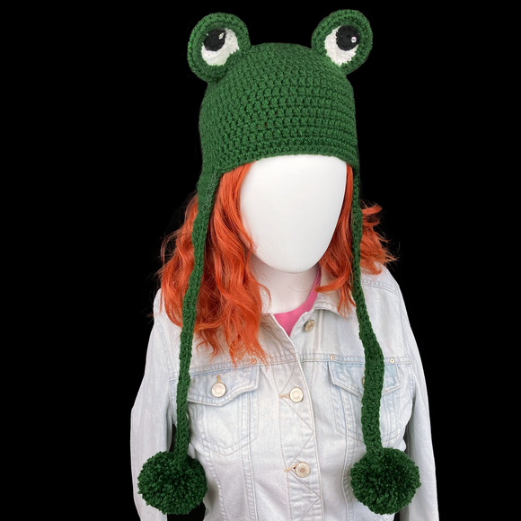 Dark forest green crochet earflap hat with frog eyes at the top of the hat and pom poms at the ends of the earflap ties. Froggy Earflap Beanie by VelvetVolcano