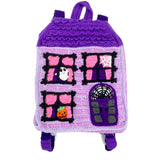 Lilac crochet Haunted House backpack with lavender brick pattern, black window frames with bubblegum pink curtains, a violet scalloped roof, a dark purple door and pumpkin, ghost and spider web accents to the window. The bag also has violet, white, black and dark purple striped straps. Haunted House Backpack by VelvetVolcano