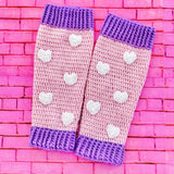 Baby pink crochet leg warmers with white heart pattern and lilac cuffs by VelvetVolcano. Background is pink brick.