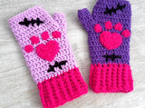 A set of crochet fingerless gloves with a Frankenstein's Monster & Zombie Cat inspired design, with one lilac glove, one violet glove, black embroidered stitch details and hot pink heart shaped paws and cuffs - NecroKitty Fingerless Gloves by VelvetVolcano