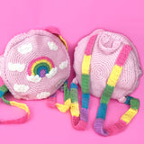 Two VelvetVolcano Pastel Rainbow Cloud Backpacks in Baby Pink, one is facing towards the camera to show the front design and the other is facing away from the camera to show the pastel rainbow striped straps.
