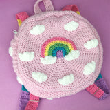 A kawaii baby pink crochet circular backpack with a cloud and pastel rainbow rainbow design and pastel rainbow striped straps. Pastel Rainbow Cloud Backpack (Baby Pink) by VelvetVolcano