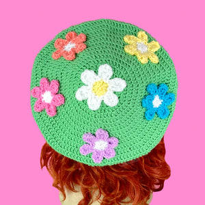 Pastel green crochet beret with 6 daisy appliques, a standard white and yellow daisy in the centre with Peach, Pastel Yellow, Turquoise, Lilac and Bubblegum Pink daisies (all with white centres) in a circle around the centre daisy. Pastel Rainbow Daisy Daze Beret by VelvetVolcano