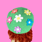 Pastel green crochet beret with 6 daisy appliques, a standard white and yellow daisy in the centre with Peach, Pastel Yellow, Turquoise, Lilac and Bubblegum Pink daisies (all with white centres) in a circle around the centre daisy. Colourful Kawaii Pastel Rainbow Daisy Daze Beret by VelvetVolcano
