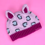 Baby pink crochet cat ear hat with dark pink inner ears and bottom rib and light grey and dark grey leopard print on the baby pink main part of the hat. Leopard Kitty Beanie (Custom Colour) by VelvetVolcano