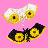 Two crochet Peter Pan style collars with a sunflower design, the first one is a champagne white colour and the second is black. Both collars feature crochet sunflower appliques on the lapels of the collar and a buttercup yellow scallop trim around the bottom edge. Sunflower Collar by VelvetVolcano