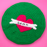 Emerald green crochet beret with cerise / hot pink heart in the centre and a white tattoo style banner over the top that says "bean" in black embroidered text. Love Heart Banner Beret (Custom Colour / Text) by VelvetVolcano