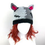 Half light grey, half dark grey crochet beanie with cat ears (which are hot pink inside) and a black ribbed brim, designed to look like a Frankenstein's Monster Kitty. Custom Colour FrankenKitty Beanie by VelvetVolcano