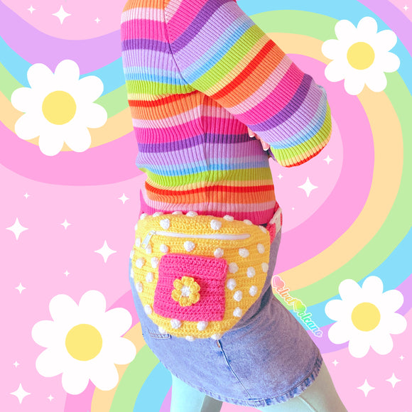 A woman wearing a pastel rainbow striped top, light denim mini skirt, pastel green leggings and a yellow polka dot crochet bum bag with bubblegum pink front pocket with a daisy on it and bubblegum pink strap