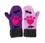 A set of crochet mittens with a Frankenstein's Monster & Zombie Cat inspired design, with one lilac mitten, one violet mitten, black embroidered stitch details and cuffs and hot pink heart shaped paws - NecroKitty Mittens by VelvetVolcano