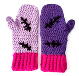 A set of crochet mittens with a Frankenstein's Monster & Zombie Cat inspired design, with one lilac mitten, one violet mitten, black embroidered stitch details and hot pink heart shaped paws - NecroKitty Mittens by VelvetVolcano