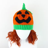 Halloween inspired orange crochet hat with contrasting neon green ribbed bottom section, neon green stem and a black carved jack o' lantern face on the main part of the hat. Pumpkin Beanie by VelvetVolcano