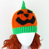 Halloween inspired orange crochet hat with contrasting neon green ribbed bottom section, neon green stem and a black carved jack o' lantern face on the main part of the hat. Pumpkin Beanie by VelvetVolcano