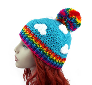 Turquoise crochet beanie with white cloud print, rainbow pom pom and rainbow rib section at the bottom of the hat. Bright Rainbow Cloud Pom Pom Beanie by VelvetVolcano