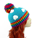 Turquoise crochet beanie with white cloud print, rainbow pom pom and rainbow rib section at the bottom of the hat. Bright Rainbow Cloud Pom Pom Beanie by VelvetVolcano