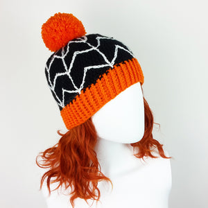 Black crochet bobble hat with white cobweb design, orange pom pom and orange bottom rib. Spider Web Pom Pom Beanie (Custom Colour) by VelvetVolcano