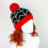 Black crochet bobble hat with white cobweb design, red pom pom and red bottom rib. Spider Web Pom Pom Beanie (Custom Colour) by VelvetVolcano