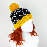 Black crochet bobble hat with white cobweb design, yellow pom pom and yellow bottom rib. Spider Web Pom Pom Beanie (Custom Colour) by VelvetVolcano